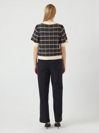 Maglione a maniche corte con motivo a quadri bianco e nero, con dettagli color crema, abbinato a pantaloni neri a vita alta e tacchi.
