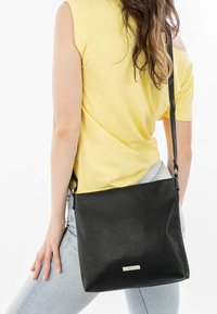 Borsa a tracolla nera in pelle con superficie texturizzata, forma rettangolare e tracolla regolabile. Presenta una placca con logo in argento sulla parte anteriore.