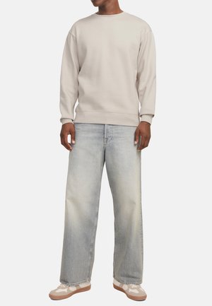 Lichtbeige sweatshirt met ronde hals; gecombineerd met lichtblauwe wijde jeans. Schoenen hebben een ontwerp in beige en wit met rubberen zolen.