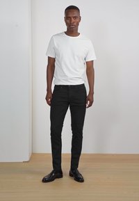 T-shirt blanche à manches courtes, jean noir slim-fit et chaussures de ville noires brillantes. Design simple ; texture lisse ; pas de motifs ou d'accents visibles.