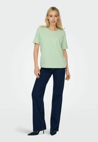 Lys grøn kortærmet t-shirt parret med mørkeblå brede jeans og spidse sorte hæle. Simpelt design, glat overflade, afslappet pasform.