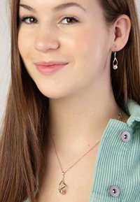 Silberohrringe mit Tropfenform und Perlenakzenten; passende Silberkette verfügt über eine spiralförmige Form und einen kleinen Edelstein. Weiches, grünes Corduroy-Oberteil.