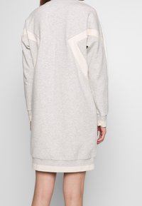 Hellgraues Sweatshirtkleid mit überschnittenen Schultern, cremefarbenen Akzenten und gerippten Bündchen. Das Kleid hat eine lockere Passform und eine Länge bis zur Mitte des Oberschenkels. Sanfte Textur.