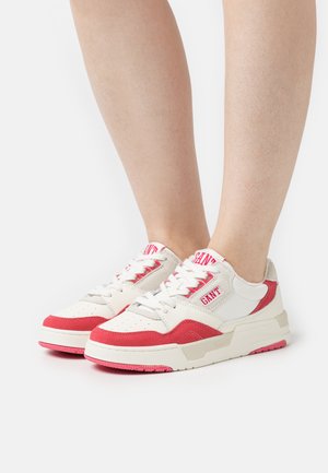 Sneakers in white and red, featuring a smooth leather upper and suede accents. Thick white sole with pink detailing and logo on tongue.