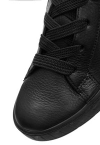Black leather sneaker with textured upper and round toe. Features flat black laces and textured rubber sole, emphasizing durability and grip.