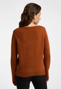 Rustfarvet sweater med rund halsudskæring, lange ærmer og ribbestrikket kant. Blød tekstur med en afslappet pasform, ingen synlige mønstre eller hardware.