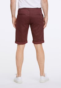 Burgundy shorts med uppvikta fållar, tillverkade av bomull, med två bakfickor och en liten logodetalj. Matchas med vita sneakers.