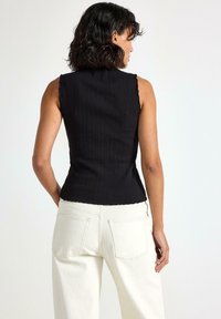 Sort ribbet tanktop uden ærmer med en bølget halsudskæring, parret med høj talje, off-white vide bukser med baglommer.