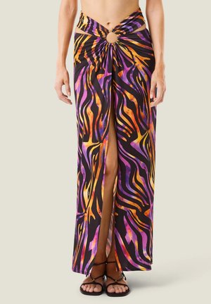 Donna che indossa una gonna lunga con spacco alto sul davanti, motivo astratto colorato in viola, arancione, giallo e nero e dettaglio centrale ad anello in vita.