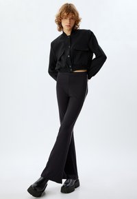 Zwarte cropped bomberjack met twee voorzakken, gecombineerd met strakke zwarte flared pants. Het materiaal lijkt glad met een subtiele glans.