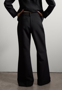 Pantalons larges noirs avec une finition en tissu lisse. Comprend deux poches arrière et une coupe ajustée, avec un détail de ourlet roulé.