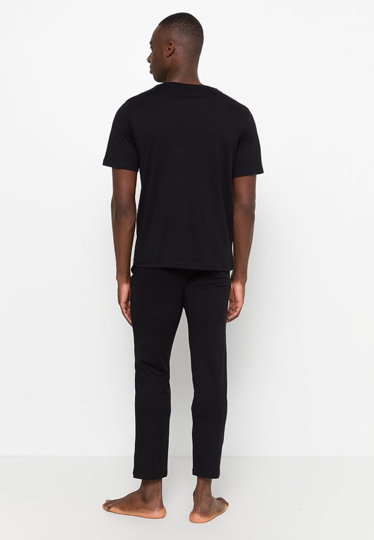 Camiseta negra de algodón y pantalones exhibidos desde la parte de atrás. La camiseta presenta un cuello redondo estándar; los pantalones tienen un ajuste slim y son de longitud hasta el tobillo.