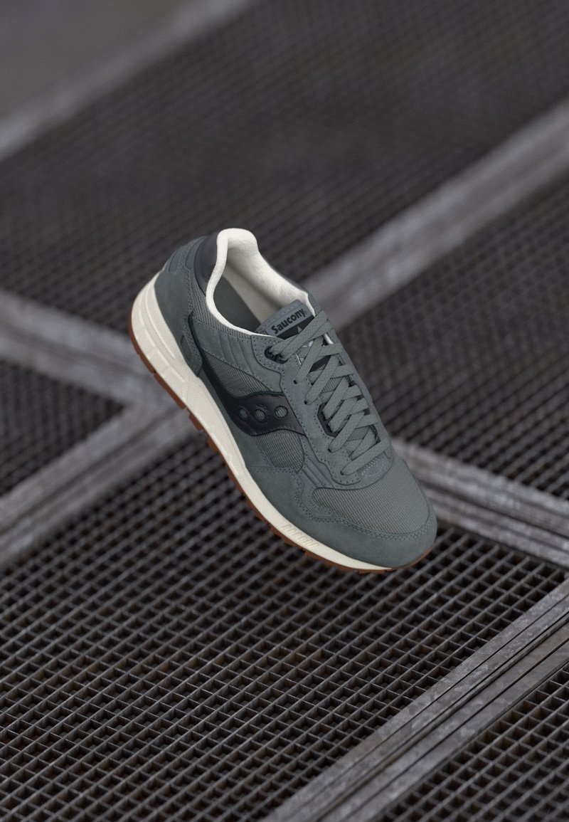 Grå sneakers med en tekstureret overdel, sorte accenter og en hvid inderside. Har en gummisål med et brunt dækmønster og stylet snørebånd.