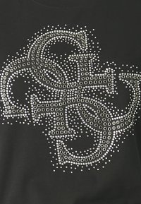 Camiseta negra con un gran diseño hecho de piedras brillantes plateadas, formando letras estilizadas, con un aspecto texturizado y brillante.