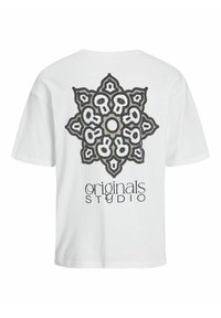 Bílý bavlněný tričko s velkým černým a kovovým geometrickým mandalovým designem na zadní straně, pod kterým je text "originals STUDIO".