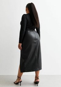 Zwarte faux leren rok, midi-lengte, aansluitend ontwerp, gladde textuur, achterkant met split, gecombineerd met zwarte bandjeshakken.