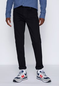 Schwarze Jeans aus Denim, slim fit mit hochgerollten Säumen. Kombiniert mit grauen, blauen und roten Sneakers, die eine Mesh- und Wildlederstruktur aufweisen.