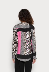 Blus med lång ärm som har en blandning av djurtryck och tydliga rosa accenter, med ett svart randmönster och en rundad nederkant.