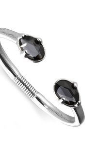 Brazalete de plata con dos piedras preciosas negras en forma de pera, textura lisa y pulida con detalles retorcidos en la banda.