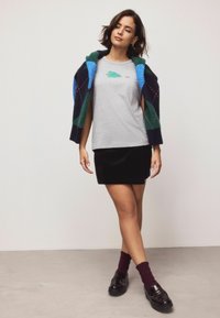 Sivý tričko s harmonickou grafikou zeleného stromu, čierna sametová sukňa a farebný pletený kardigán prehodený cez plecia; čierne mokasíny a bordové ponožky.