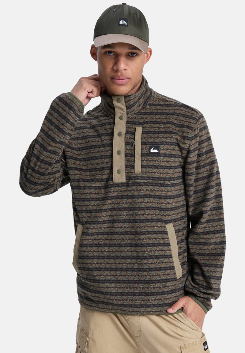 Καφέ και πράσινο φλις με μοτίβα, μπλούζα με μισό φερμουάρ στο λαιμό και κλείσιμο με κουμπιά. Διαθέτει δύο πλαϊνές τσέπες και ετικέτα με λογότυπο.