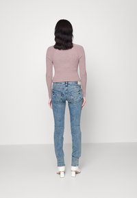 Světle růžový vrúbkovaný top s dlouhým rukávem v kombinaci se středně modrými úzkými džíny. Džíny mají zadní kapsy se zdobícím prošitím a vybledlý vzhled.