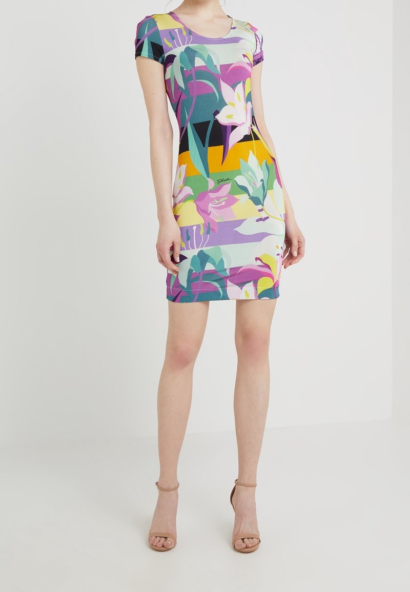 Femme portant une robe à manches courtes, longueur genou, avec un motif floral et abstrait coloré, associée à des talons ouverts beige.