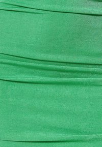 Tissu vert avec une texture lisse, présentant des plis horizontaux et un léger relief tout au long. Uniformité de couleur avec une finition mate.