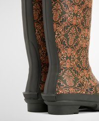 Green rubber boots feature an intricate orange floral pattern and a textured finish, with a durable sole and flexible side structure.