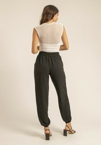 Pantalons noirs à coupe décontractée avec taille élastique, poches et ourlets. Haut sans manches blanc avec détail transparent au dos. Sandales à talons carrés.