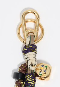 Llave metálica dorada con gancho de presión, cuerdas trenzadas de colores en púrpura, verde y crema, y un charm redondo que presenta "BIMBA VIOLA" en multicolores.