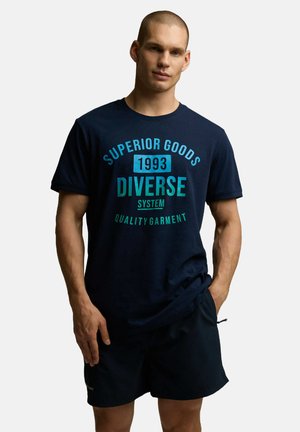 Granatowa bawełniana koszulka z nadrukiem w odcieniach cyjanowych: "SUPERIOR GOODS 1993 DIVERSE SYSTEM QUALITY GARMENT." Krótkie rękawy i luźny krój.