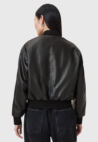Giubbotto bomber in pelle nera con vita aderente, polsini a coste e una superficie liscia, caratterizzato da un design semplice e senza marchi visibili.