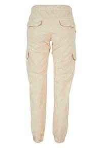 Pantalon cargo beige avec taille et poignets élastiques, poches à rabat à l'arrière et sur les côtés, vu de dos.