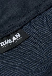 Marinblått tyg med en strukturerad mönstring, med en vit etikett som läser "IUMAN" och "intimissimi uomo." Nära vy av sömnadsdetaljer.