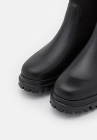 Černé voděodolné kozačky po kotníky s hladkým koženým povrchem, zaoblenou špičkou, elastickými bočními panely a robustní gumovou podrážkou s hlubokými výstupky.