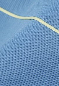 Close-up van blauw textiel met een opstaand gele golvende lijn die diagonaal over het oppervlak loopt.