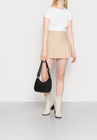 Vit kortärmad t-shirt, rutigt plisserat beige kjol, svart handväska och krämfärgade blockklackade knähöga stövlar. Enkla och moderna designelement.