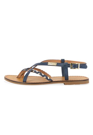 Navy blue leather sandal with braided straps, flat sole, and a buckle closure. Features a tan insole and minimalistic design elements.