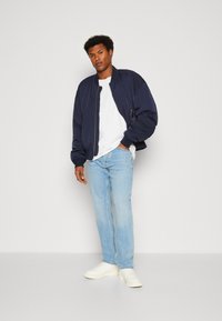 Chaqueta bomber de navy con bolsillos con cremallera, camiseta blanca, jeans azul claro y zapatillas blancas. Textura suave, corte relajado y estilo casual.