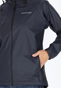 Navy blue waterproof jacket with a zip front, adjustable hood, and side pockets; features smooth texture and a logo on the chest.