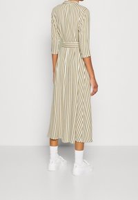 Raidallinen midi-mekko vaaleanbeigeinä ja kermanvärisinä, jossa on kolmen neljänneksen hihat, istuva vyötärö ja virtaava hame. Yhdistetty valkoisiin lenkkareihin.