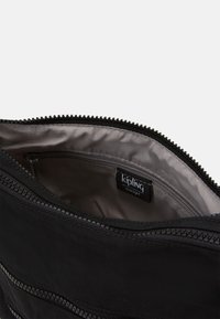 Schwarze Nylon-Tasche mit einem Reißverschluss, ausgestattet mit einem glatten Innenfutter und einer kleinen Innentasche. Markenlabel innen sichtbar.