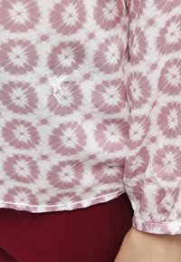 Blusa rosa chiaro con motivo floreale bianco, caratterizzata da una vestibilità ampia e maniche lunghe, realizzata in tessuto leggero. Cuciture decorative all'orlo visibili.
