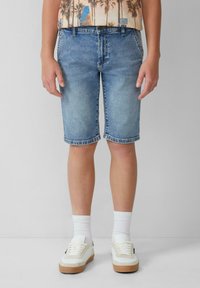 Shorts en denim bleu clair avec une coupe droite, bords finis et cinq poches. Associés à des chaussettes blanches et des baskets.