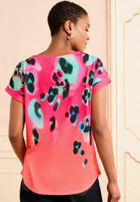 Krátky rukáv top v ružovej tkanine s leopardím vzorom v čiernej, modrej a zelenej farbe, s okrúhlym výstrihom a voľným strihom.