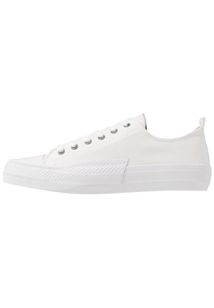 Hvid lærreds-sneaker i lav model med hvid gummisål, metaløjer, hvide snørebånd og tekstureret tåhætte, vist på en hvid baggrund.