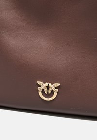 Borsa in pelle marrone con finitura testurizzata e un accento in metallo dorato a forma di due uccelli con le ali.