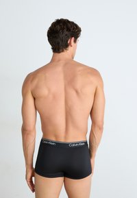 Zwarte boxershorts van een zachte elastische tailleband met "Calvin Klein" in witte tekst, ontworpen voor een snug, comfortabele pasvorm.
