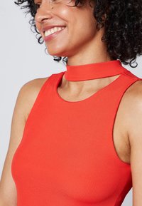 Top senza maniche a costine rosso con scollo a choker e tagli sulle spalle. Il tessuto è liscio ed elastico, esaltando la forma del corpo.